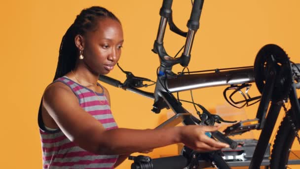 修理とメンテナンスを待っているスタジオの背景に損傷した自転車を分析する手のタブレットを持つエンジニア 修理スタンドで自転車を診断するために電子デバイスを使用している女性 カメラA — ストック動画