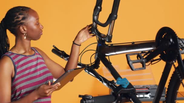 非洲裔美国妇女在工作室的后台维修车间做自行车维修 查看平板电脑维修清单 技师检查需要修理的自行车部件 照相机A — 图库视频影像