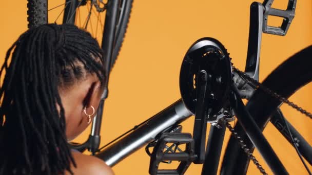 アフリカ系アメリカ人女性がペダルを押して自転車の車輪を回転させ それを検査し ドライバーと六角ソケットレンチを使ってそれを修正し ショットを閉じます 乗馬趣味のテスト自転車クランクアームとチェーンリング — ストック動画