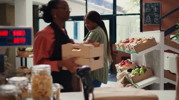 アフリカ系アメリカ人のクライアントは 瓶からさまざまなバルク製品を注ぎ 再利用可能な容器に保管された有機自家製商品を購入しました 市場でバイオアイテムを選択するビーガン女性 ハンドヘルドショット — ストック動画