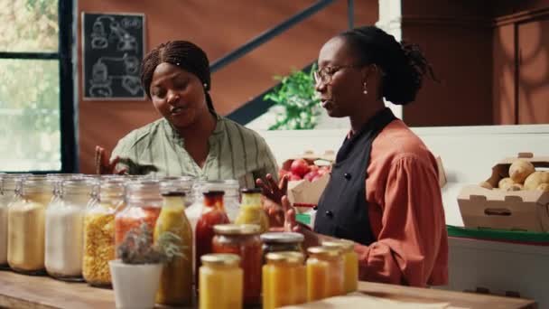 バイヤーに自家製ソースとドレッシングを示すベンダー ビーガン栄養と健康的なライフスタイルを促進 地元の食料品店で天然バルクアイテムを提示する小売業者 ハンドヘルドショット — ストック動画