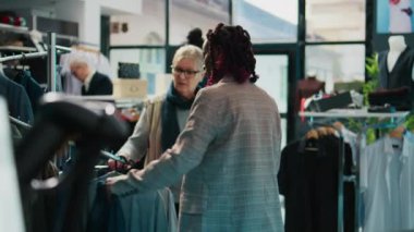 Afro-Amerikan perakende katibi alışveriş merkezindeki mağazadaki üst düzey müşteriye yeni moda koleksiyonunu gösteriyor. Hamilelik asistanı düzenli müşteriye renk önerisinde bulunuyor. Tüketim. Kamera B.