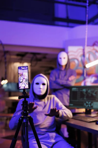 Anonymous criminals streaming web threat on smartphone, doing cyberattack. Hackers committing internet crime while recording fraud video on mobile phone and asking victim for payment