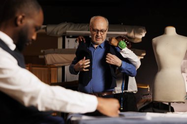 Önemli iş toplantısından önce özel yapım şık takım yelek deneyen kıdemli müşteri. Yaşlı işadamı deneyimli bir terzinin yardımıyla el yapımı giysilere bakıyor.