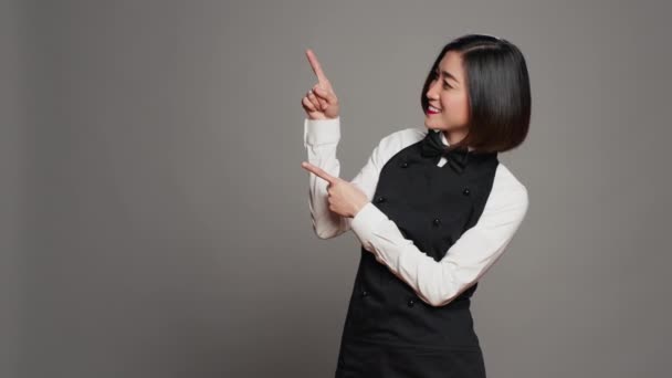 亚洲女服务员指着工作室里的广告 指指她头顶上方的方向 以创建促销广告 餐饮业的女员工指向一些向上的东西 相机A — 图库视频影像