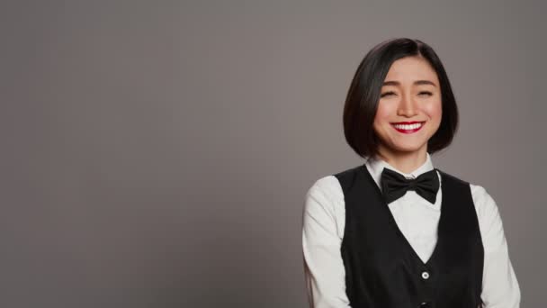 アジアの女性ホテルのコンシェルジュは 受付としてホスピタリティ業界で働く弓でエレガントな制服を着ています レセプション デスク管理者挨拶クライアント 灰色の背景 カメラ — ストック動画
