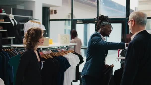 非洲裔美国人工人穿着黑色衬衫 打着红领结 帮助他为优雅的场合购买完美的服装 专业的造型师给商店里的买主提建议 摄像头B — 图库视频影像