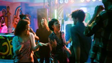 Gençler gece kulübünde eğleniyor, elektronik müzik eşliğinde dans ediyor. Neşeli insanlar partiden zevk alıyor ve diskotekte dans figürleri gösteriyor, canlı performans. El kamerasıyla..