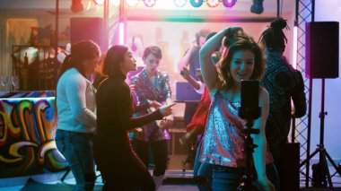 Mutlu kız internet için video kaydediyor, dans pistindeki diskotekte cep telefonu kullanıyor. Kadın nüfuzlu biri, dans eden, zıplayan ve disko yapan insanların videolarını çekiyor. El kamerasıyla..