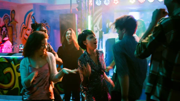 Gençler gece kulübünde eğleniyor, elektronik müzik eşliğinde dans ediyor. Neşeli insanlar partiden zevk alıyor ve diskotekte dans figürleri gösteriyor, canlı performans. El kamerasıyla..