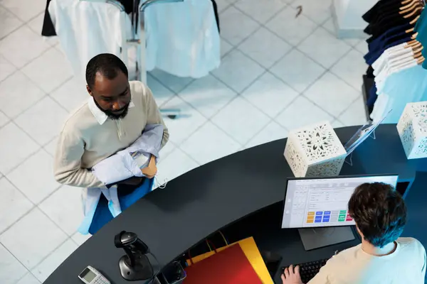 買い手がチェックアウトトトップビューに並んでいる間 コンピュータで現金登録ソフトウェアを使用して衣料品店の労働者 ショッピングセンターの従業員 顧客が待っている間カウンター デスクで働くキャッシャー — ストック写真