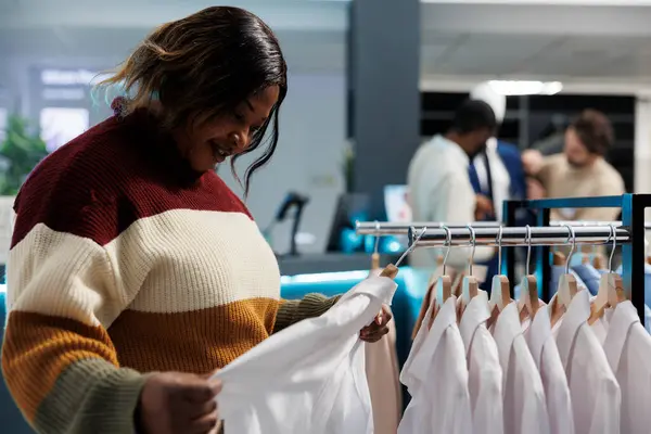 適合を点検する白いシャツの生地の質を点検する衣類の店のバイヤー アフリカ系アメリカ人女性は 正式なウェアを掛けてラックをブラウジングし ブティックでアパレルサイズを選択 — ストック写真