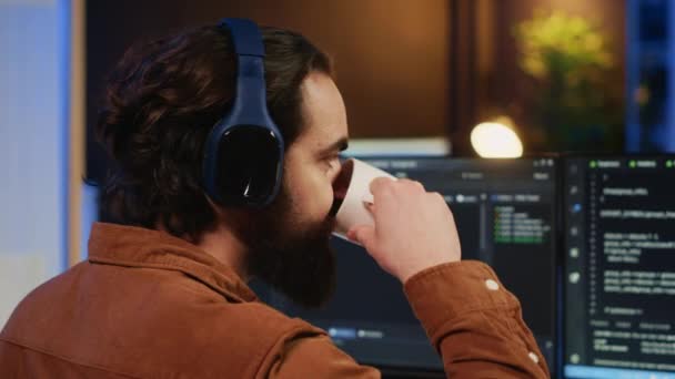 男人在办公室做It辅助工作 边喝咖啡边听音乐边编代码 有耳机的开发人员可以在电脑上享用热茶和编写代码 相机近视 — 图库视频影像