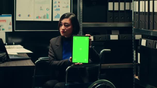 車椅子の法律エージェントは 障害のあるアーカイブルームのデバイス上の隔離されたモックアップレイアウトを使用して タブレット上の緑色のディスプレイを示しています 染色体スクリーン付きのガジェットを保持する調査員 カメラ — ストック動画