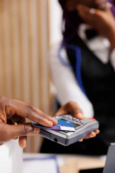 Hotel guest using credit card to pay for stay while registering at front desk, close up. Male hand making contactless payment during check-in, paying for room with nfc technology