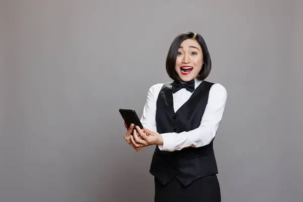 Podekscytowana Azjatycka Recepcjonistka Hotelowa Mundurze Trzymająca Smartfona Patrząca Kamerę Zaskoczona — Zdjęcie stockowe