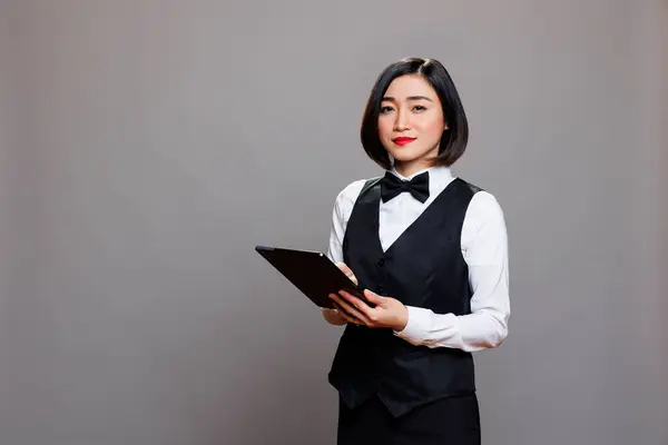 微笑自信的亚洲女服务员穿着专业制服 手持数码平板电脑 看着相机 年轻迷人的接待行业接待员使用便携式小玩意肖像 — 图库照片