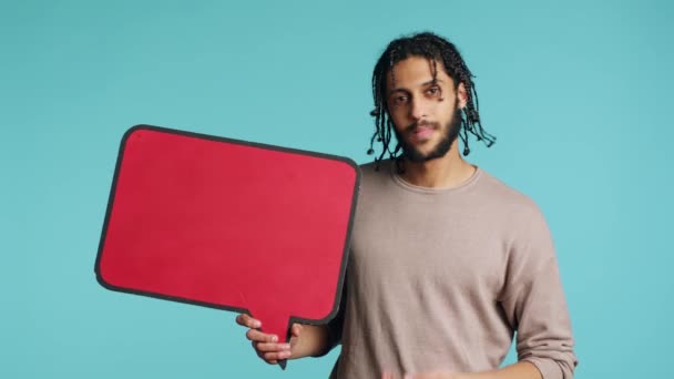 快乐的男人拿着红色的语音泡泡符号空白处的文字 快乐的中东人展示着思想泡泡纸板 隔离在蓝色的工作室背景下 — 图库视频影像
