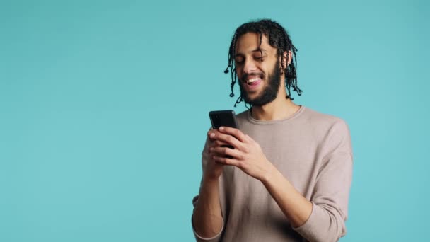 Bipoc男人用智能手机发短信给最好的朋友 笑着讲笑话 在与伴侣在手机上聊天 在工作室背景上与伴侣隔离 相机A聊天时放松的人 — 图库视频影像