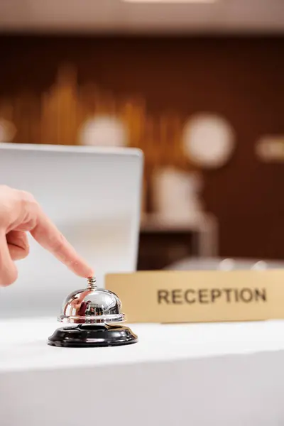 Traveller calling for hotel concierge with service bell on front desk counter, ringing bell to do check in. Hotel guest looking to relax before attending upcoming business meeting. Close up.