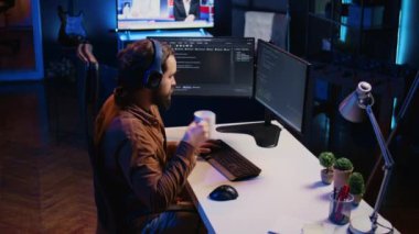 Uzaktan kumandalı ofis vardiyası sırasında müzik dinleyip kahve içen geliştirici. IT uzmanı ses yayını ve sıcak içecekten keyif alıyor, bilgisayar ve kamera B üzerinde çalışıyor.
