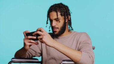 Özürlü bir adam cep telefonuyla yoğun video oyunu oynar, dokunmatik ekranda spam saldırı tuşları kullanır. Oyuncu tekerlekli sandalyede, stüdyo geçmişinde, B kamerasında oyun yarışmasına katılıyor.