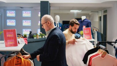 Perakende mağazasından alışveriş yapan çeşitli insanlar, ürünlerde kırmızı siyah cuma indirim etiketi arıyorlar. Moda mağazasında elbise askılarını arayan müşteriler butiği keşfediyorlar..