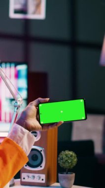 Dikey Video Afrikalı Amerikalı kız evde izole edilmiş yeşil ekranlı bir telefon tutuyor, üniversitede ekonomi ve finans okuyor. Genç bir kadın çalışırken boş bir şablon kullanır.