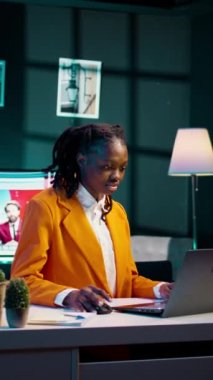 Dikey Videolu Kadın özenle ev ofisinin konforunda dizüstü bilgisayarda yazıyor, üniversite ödevini bitirmek için okul ödevi yazıyor. Afrikalı Amerikalı öğrenci gelişim üzerine çalışıyor.