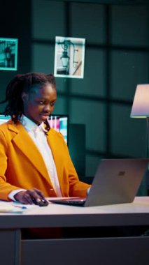 Dikey Video Afrikalı Amerikalı öğrenci, evde bekar ödevi üzerinde çalışıyor, online araştırmalardan fikirler yazıyor. Ek bilgi için dijital kütüphaneleri ve akademik veritabanlarını araştıran kız