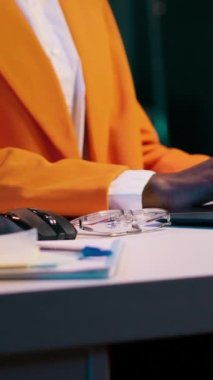 Afro-Amerikan öğrencilerin dikey video portresi gözlük takıyor ve evde İngilizce kompozisyonlar üzerinde çalışıyor, ek kaynaklar için akademik veri tabanlarını okuyor. Üniversitede okuyan genç bir kadın.
