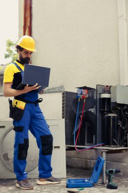 Dışarıdaki klima rutin kontrolleri için sertifikalı uzman görevlendirildi. Bilgisayara veri yüklüyor. Eğitimli tamirci Hvac sistem güvenlik kontrolü yapıyor, arızalı iç parçaları arıyor
