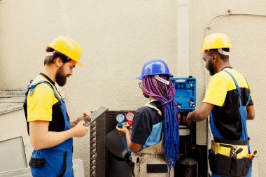 Uzman tamirciler ve ev sahibi tarafından sıcak yaz aylarında kötü soğutma sorunlarına yol açan yoğunlaştırıcı buharlaştırıcı bobinlerindeki freon sızıntılarını araştırmak için tutulan Afro-Amerikan iş arkadaşları.