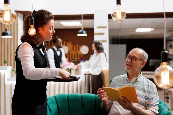Dinlenme Odasında Genç Garson Elinde Kitapla Kanepede Oturan Yaşlı Turistlere — Stok fotoğraf