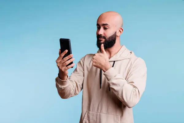 スマートフォンを使用してビデオ通話中に親指を示す若いアラブ人男性 携帯電話のビデオ会議でオンラインリモート会話をしながら承認サインを作る人 — ストック写真