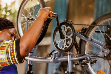 Tutkulu spor düşkünü siyah kadın bisiklet pedallarını ve zincirleri özenle inceliyor ve onarıyor. Aktif Afro-Amerikan bayan bisikletçi modern bisiklete yıllık ayarlamalar yapıyor..
