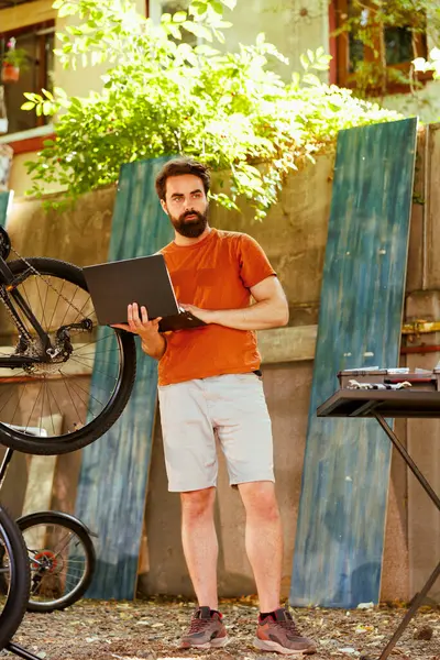 Zdrowy Oddany Biały Mężczyzna Używa Laptopa Naprawy Zepsutego Nowoczesnego Roweru — Zdjęcie stockowe