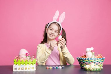 İş yerinde yumurta süsleyen, Paskalya bayramını kutlamak için el yapımı süslemeler yapan tavşan kulaklı bir delikanlı. Güzel bir çocuk süsleme yapmak için boya fırçasıyla eğleniyor..