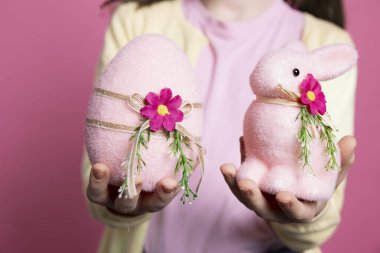 El yapımı süslemelerini, sevimli pembe yumurtalarını ve oyuncak tavşanını sunan sevimli küçük bir çocuk. Küçük kız gülümsüyor ve Paskalya kutlaması için heyecanlanıyor. Kapat..