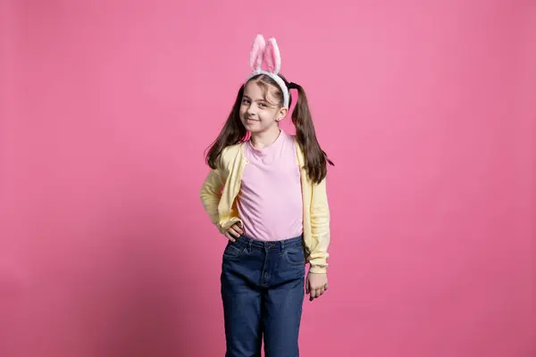 小女孩感到快乐 在镜头前跳舞 在粉红的背景下鬼鬼祟祟 年轻的蹒跚学步的孩子 长着小兔子般的耳朵 在演播室里摆出一副自信的样子 — 图库照片