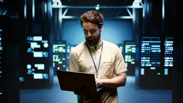System administrator walking between operational server racks in computer network security data center, ensuring optimal performance. Engineer monitoring energy consumption across components