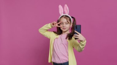 Akıllı telefon webcam 'inde fotoğraf çeken kendinden emin genç bir kız örgülü saçı ve tavşan kulaklarıyla kendini sevimli hissediyor. Neşeli gülümseyen çocuk fotoğraf çeker ve stüdyoda aylak aylak dolaşır. Kamera A.