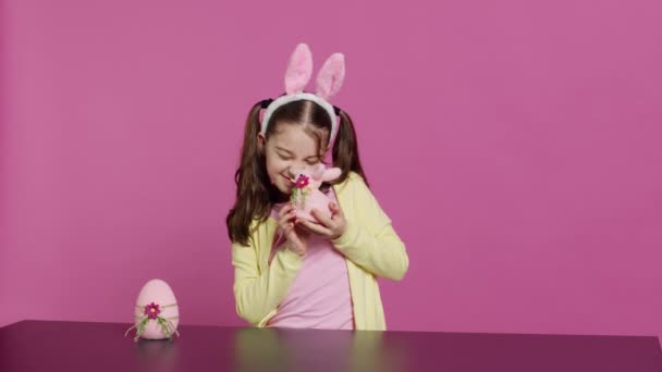 素敵なイースターの装飾で遊ぶ喜ばしい少女は 春の休日の祭りを祝うためにお祝いの装飾を作成します かわいいピンクのウサギと卵をプレゼントする陽気な子供 カメラ — ストック動画