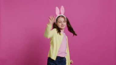 Stüdyoda dans figürleri gösteren kendinden emin neşeli bir kız Paskalya bayramı şenliği hakkında neşeli ve pozitif hissediyor. Etrafta dans eden ve tavşan kulağı takan yetenekli bir çocuk. Kamera B.