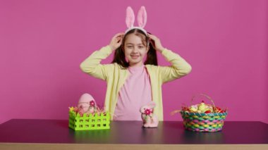 Gülümseyen, kendine güvenen bir bebek kafasına tavşan kulağı takıyor ve pembe arka plana selam veriyor. Paskalya bayramı etkinliği için süslemeler yapan sevimli, neşeli çocuk. Kamera B.