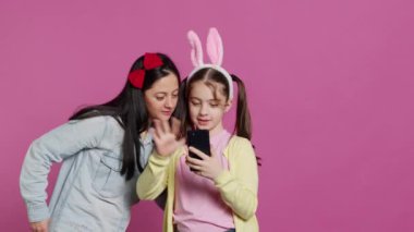 Küçük liseli kız ve annesi stüdyoda video konferansında konuşuyorlar, webcam 'e el sallıyorlar ve aileleriyle sohbet ediyorlar. Sevimli çocuk ve anne telekonferans sohbeti için akıllı telefon kullanıyor. Kamera A.