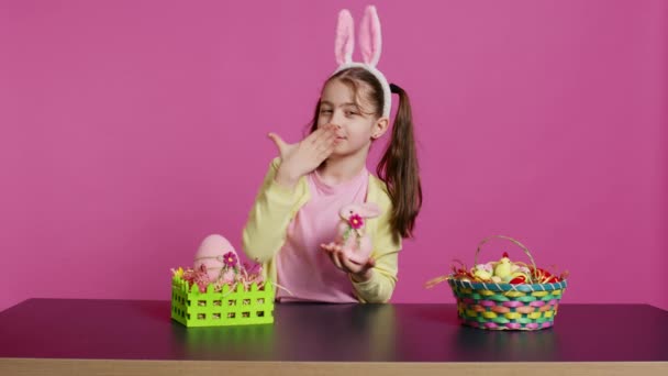 カメラの前で空気キスを吹く若い女子生徒は 詰まったウサギのおもちゃでお祝いの素敵なアレンジを作成します イースターのお祝いに興奮している陽気な子供 カメラ — ストック動画