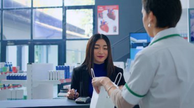 Eczanedeki Asyalı kadın eczanede tıbbi malzeme almak için kredi kartı kullanıyor. İhtiyacımız olan virüsü bulduktan sonra eczaneye ücretsiz ödeme yapan mutlu bir müşteri.