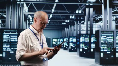 Senescent professional navigating network of server rigs in industrial nexus. Employee with tablet doing analysis and optimizations in high tech data center, preventing system perils clipart