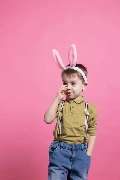 快乐的小孩在粉红的背景下自信地摆姿势 戴着小兔子耳朵庆祝复活节 小孩子在镜头前微笑着 等待着收到礼物 — 图库照片